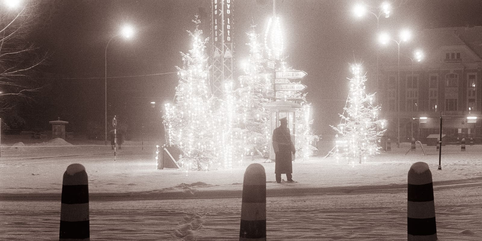 Snowy town square at night with trees glowing in holiday lights